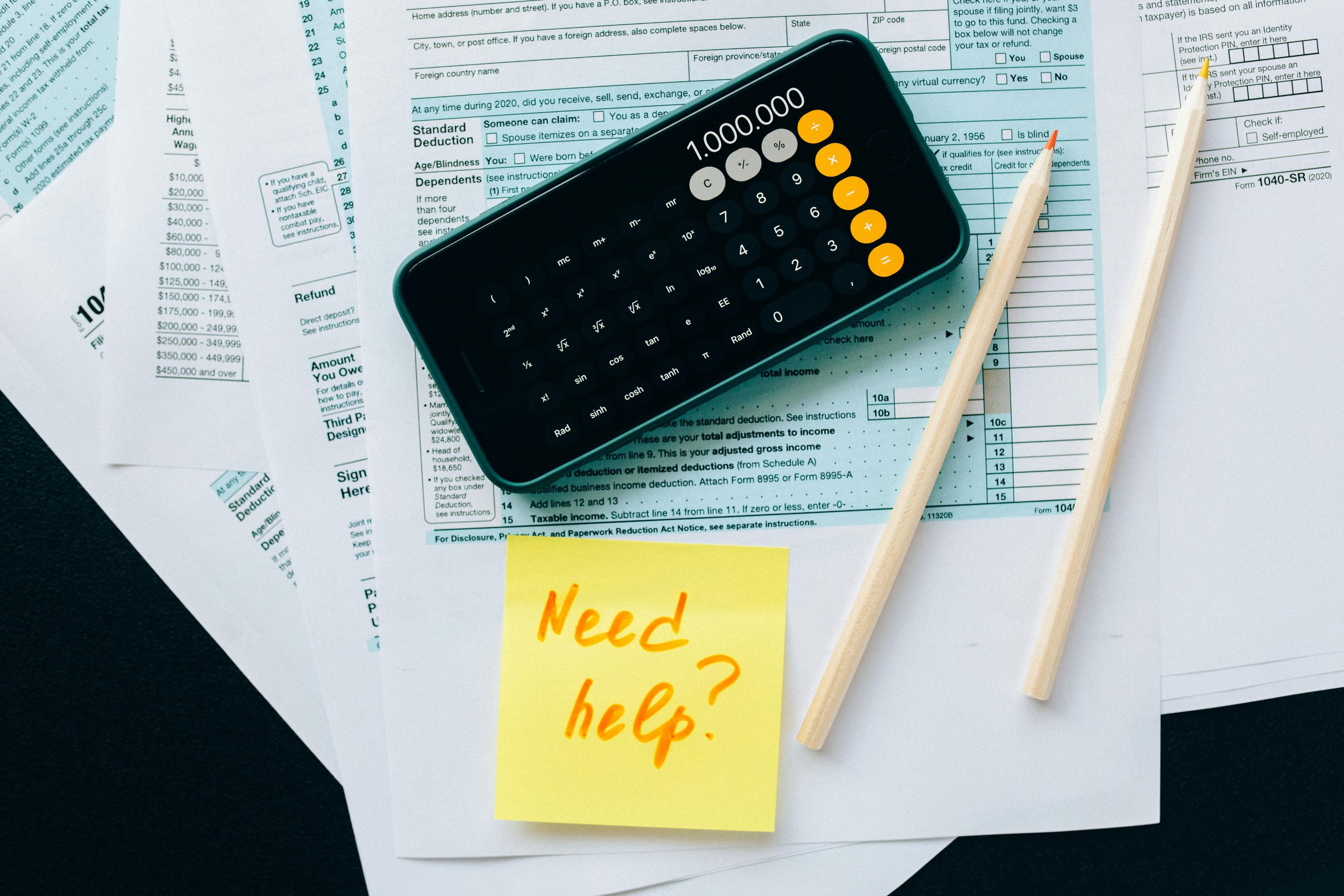 Top view of financial papers with a calculator, pencils, and a note saying 'Need help?' indicating tax or accounting assistance.